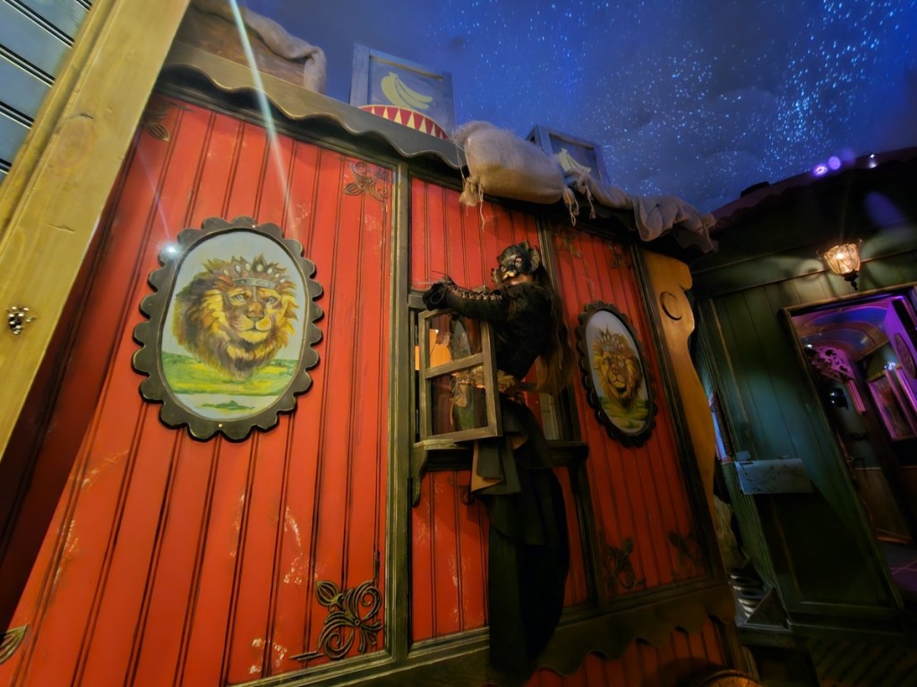 A masked character emerging from a circus caravan window.