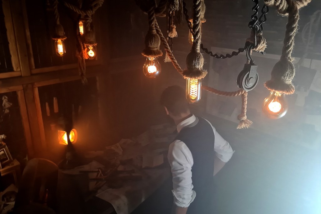 View from above of a man in a dark room looking over a table covered in papers.