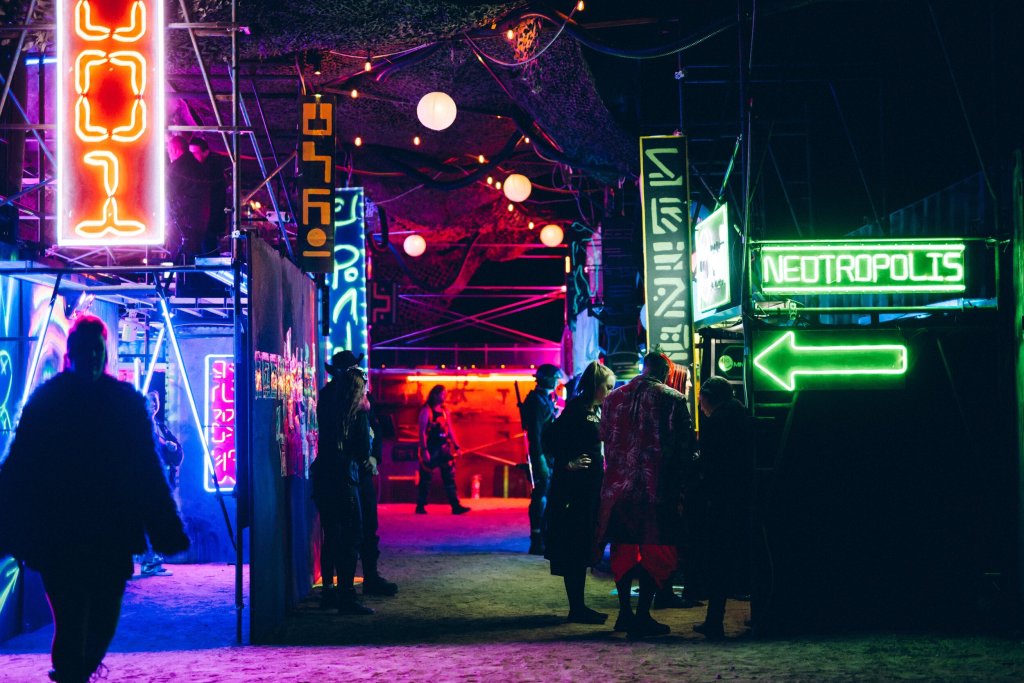scaffolding and walls with neon signs and people wandering
