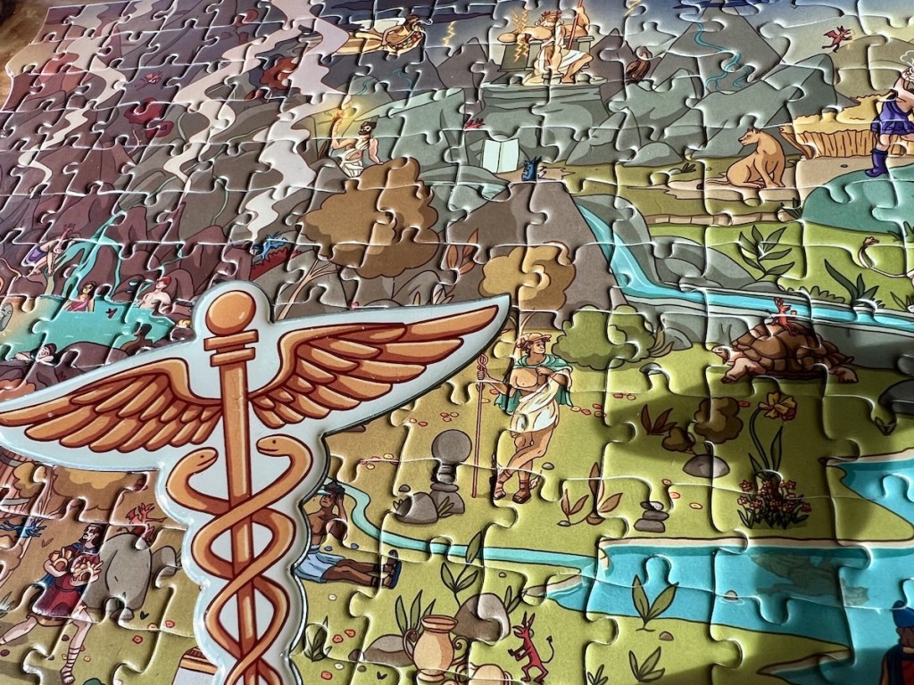 An assembled jigsaw puzzle filled with Greek gods, demigods, and monsters. A Caduceus hovers in the foreground above the puzzle, casting a shadow.