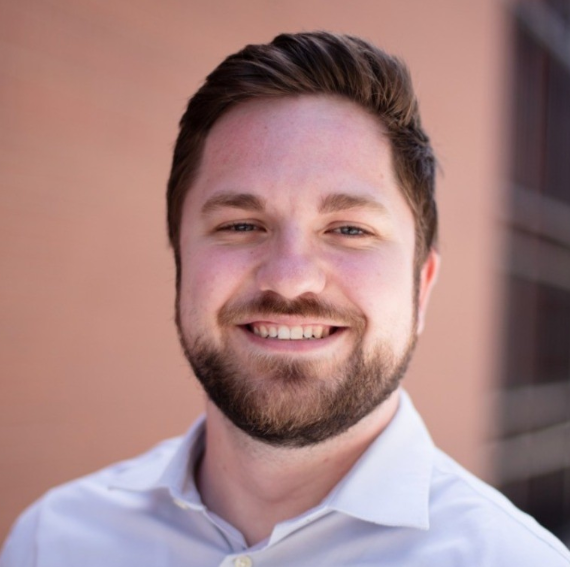 man with neat brown hair and short brown beard, smiling, in button down white shirt
