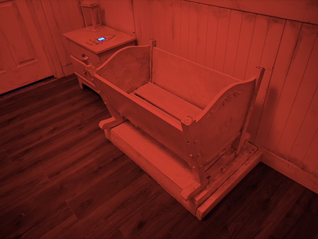 A white bassinet in a room bathed in red light.