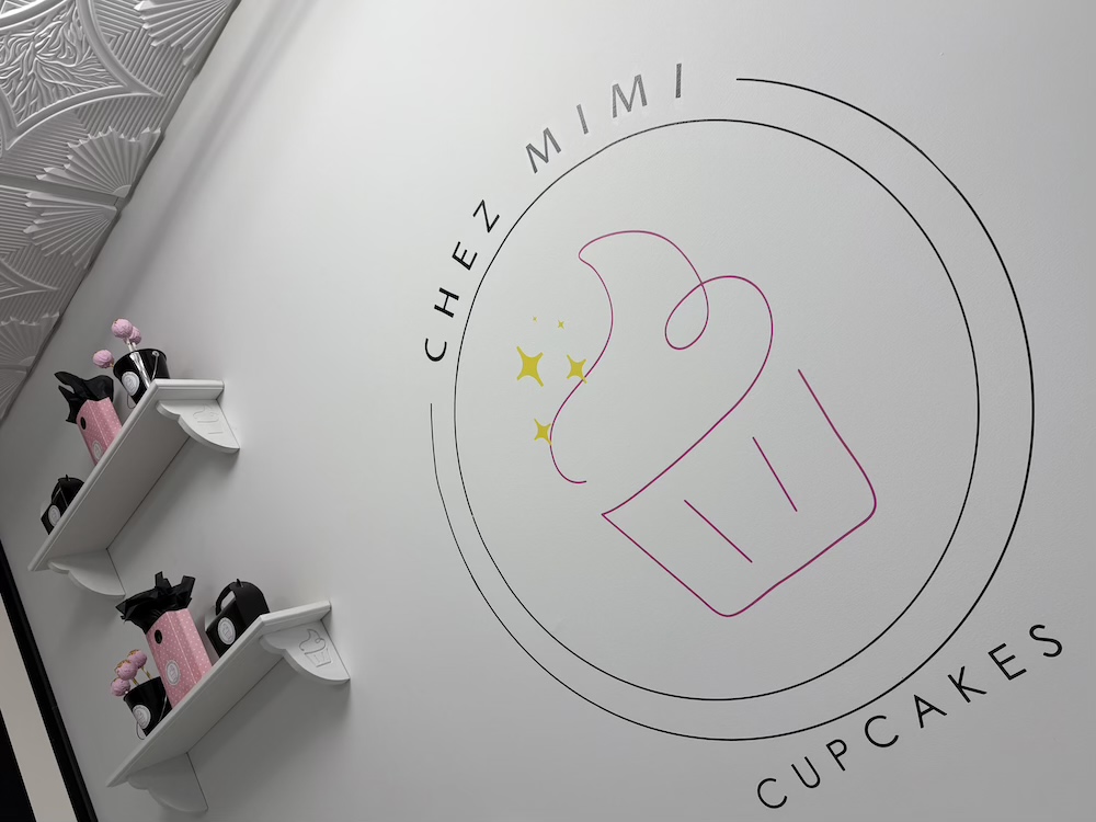 Chez Mimi Cupcakes pink and yellow sparkle cupcake logo against a white wall.