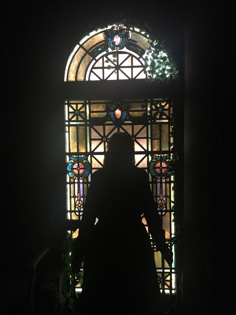 Silhouette of a woman in a dress in front of a stained glass window