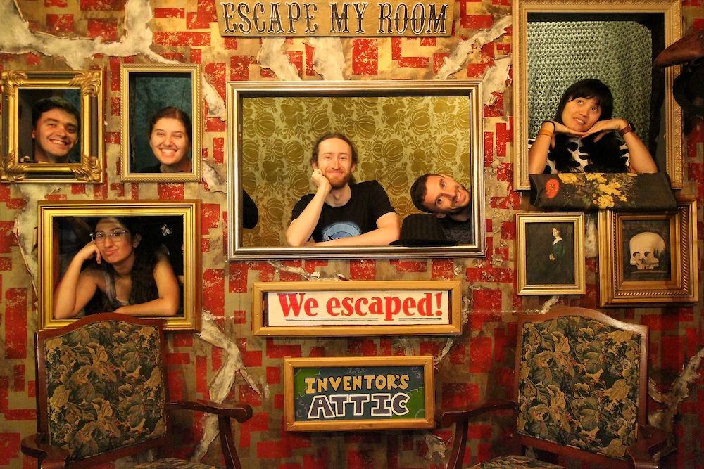 6 people standing with their heads framed within portrait frames as if they are paintings.