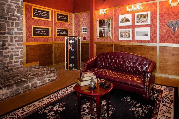 room with red leather couch, photos on walls, edge of large brick fireplace, and a steamer trunk in the back corner