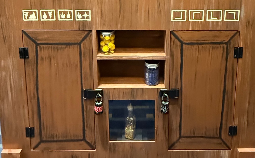 A wooden cupboard with locked doors and symbols painted around it.