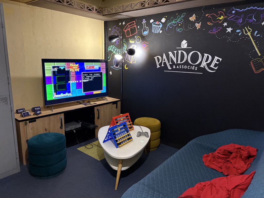 A living room-like space with a Playstation, a game of guess who, and a mural on the wall that reads, "Pandore & Associes"