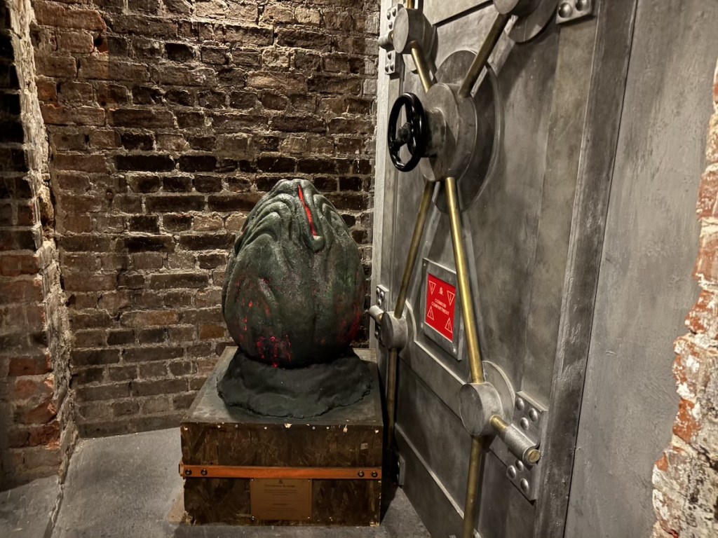 A large, metal vault door beside a strange egg-like object that looks alien in origin.