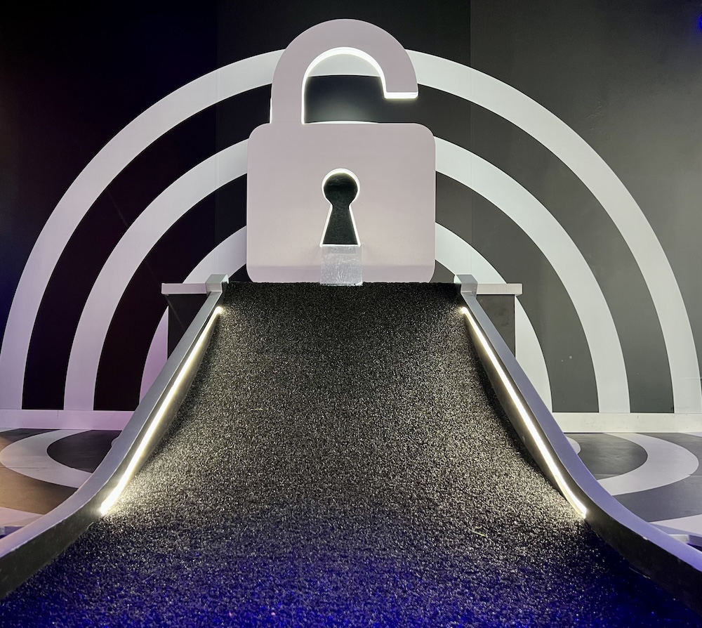 A mini golf hole with black turn and a large white padlock as an obstruction.