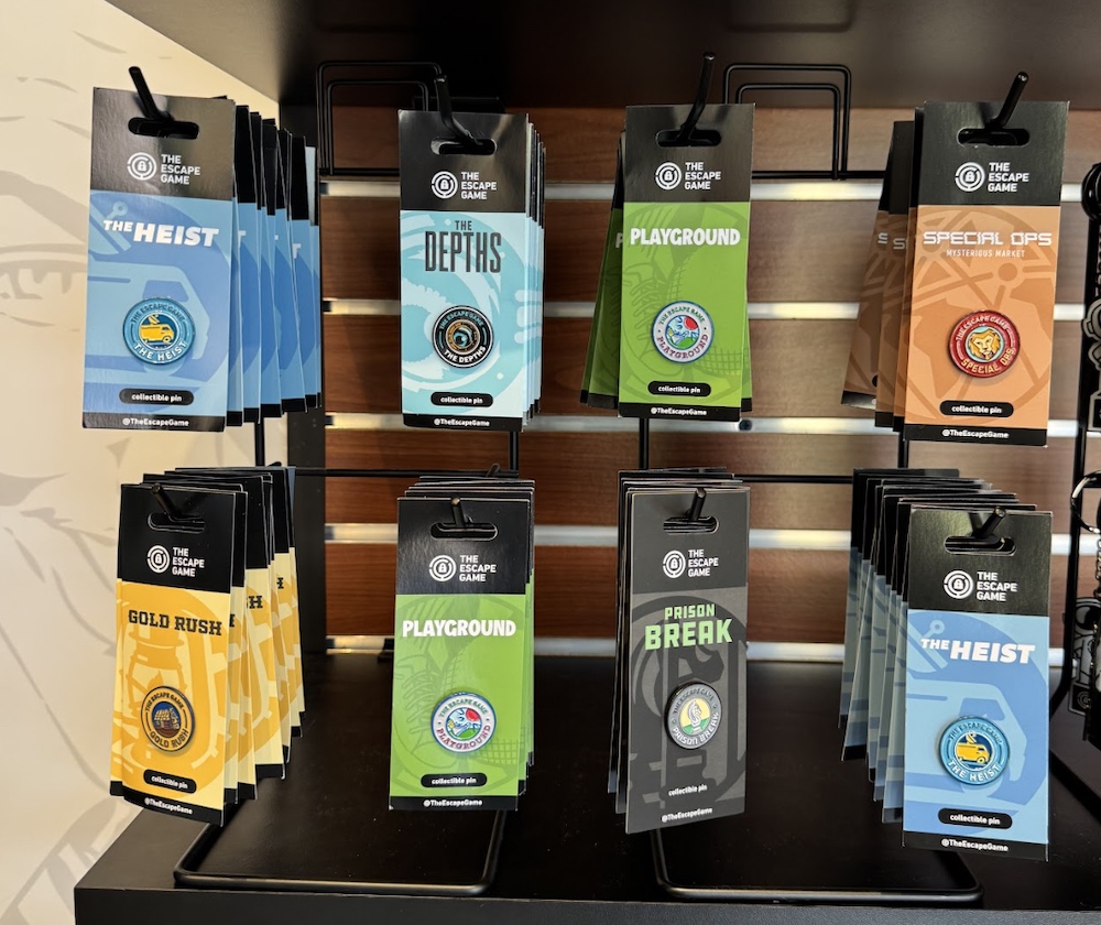 A display of 8 enamel pins, each one representing a different game at The Escape Game.