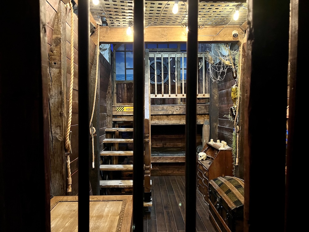 The interior of a pirate ship viewed through the bars of the ship's brig.