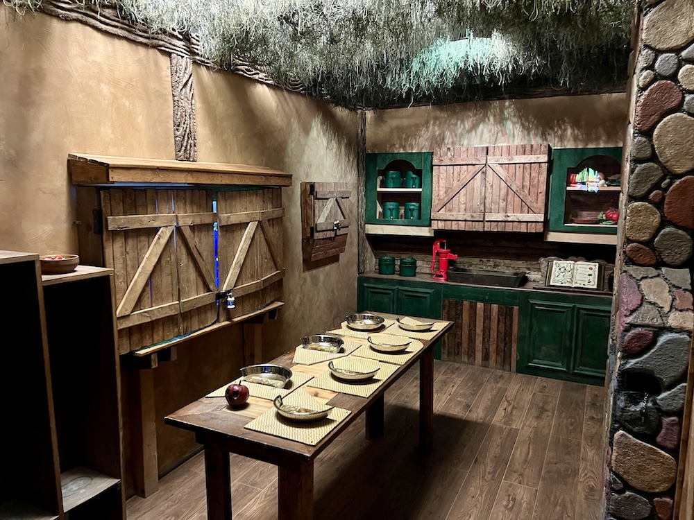The kitchen interior of a cabin with a stone chimney and a table set for 7.