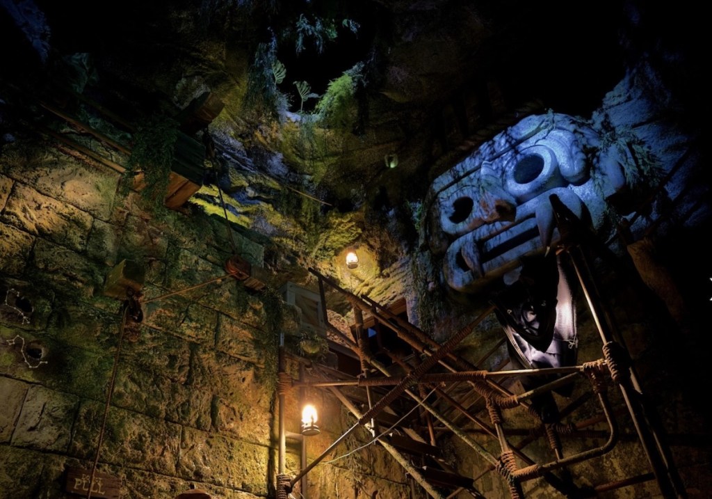 An intensely detailed excavation site in a Central American temple. A metal stairway extends up to a second level.