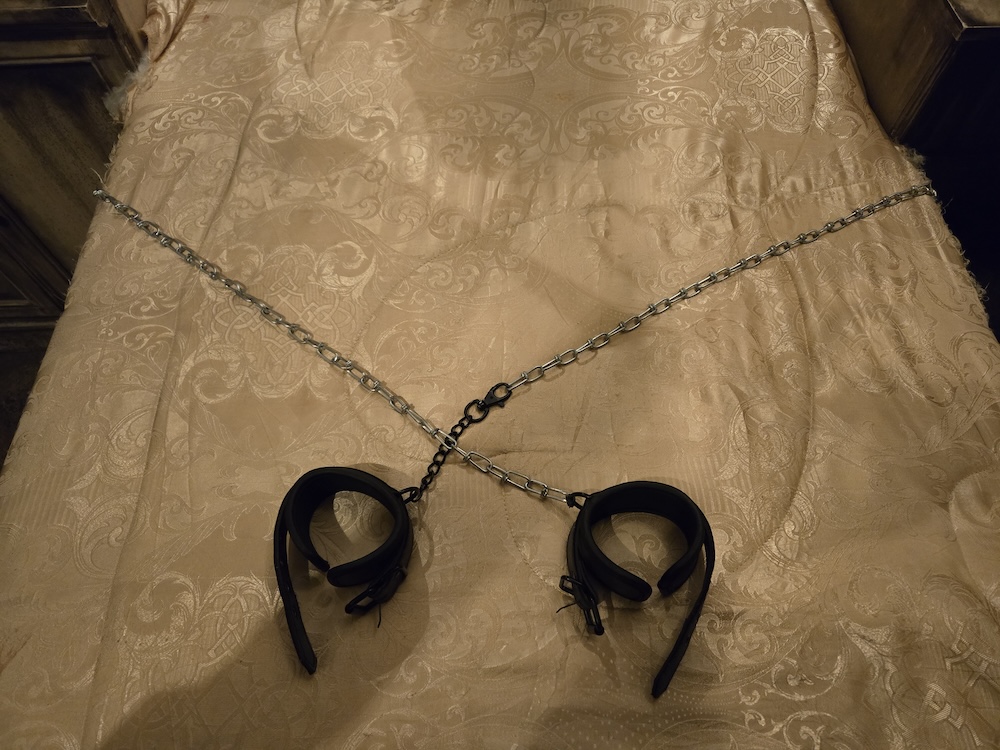 A bed with a pair of chains and cuffs laying atop.