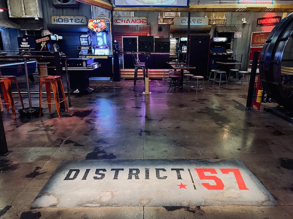 District 57 logo painted on the concrete floor, surrounded by tables and stools.