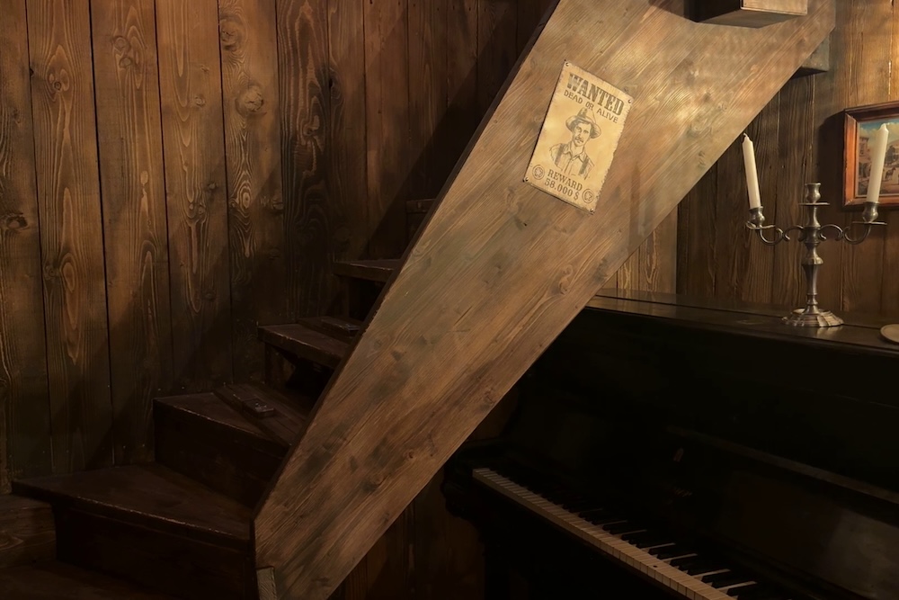 A wooden stairway with a wanted poster beside a piano inside of an old west saloon.