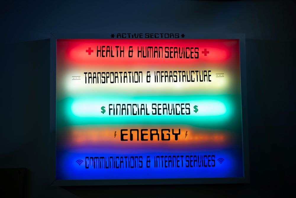 A brightly lit sign shows five "Active Sectors": Health & Human Services in red, Transportation & Infrastructure in yellow, Financial Services in green, Energy in orange, and Communications & Internet Services in blue