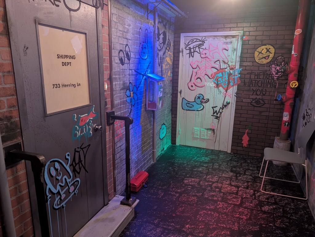Photo of a small, brick-walled room laden with graffiti, black light, and doors. The space is supposed to be an alleyway.