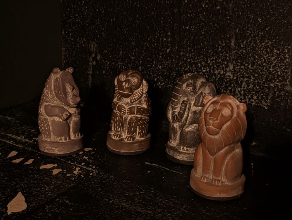 A close-up of four wooden animal figurines: a rhinoceros, a monkey, an elephant, and a lion.