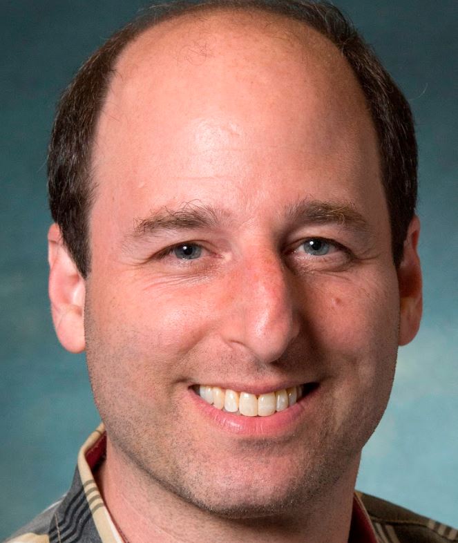 man with short brown hair and blue eyes, smiling.