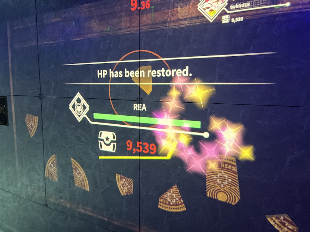 A game with floating pieces of something is projected onto a wall. A green health bar with sparkles around it lies under the text "HP has been restored." The number 9539 next to a treasure box icon appears in red.