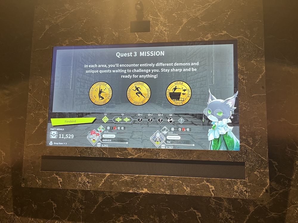 A digital screen shows the words "Quest 3 MISSION: In each area, you'll encounter entirely different demons and unique quests waiting to challenge you. Stay sharp and be ready for anything!" along with three icons. The three icons show a person jumping with music notes, a runner, and a person in a mine cart throwing a ball at some bats. On the lower portion, the cat character from earlier appears alongside a screen showing the party's progress - Quest 1 and 2 clear - and medal count.