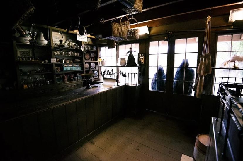 Am image of a dark antiques shop. Outside two cloaked figures stand in the doorway.