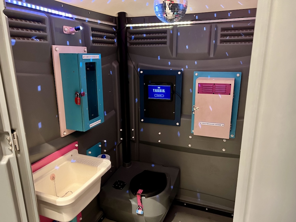 Interior of a porta-potty that has been turned into an escape room with a disco ball.
