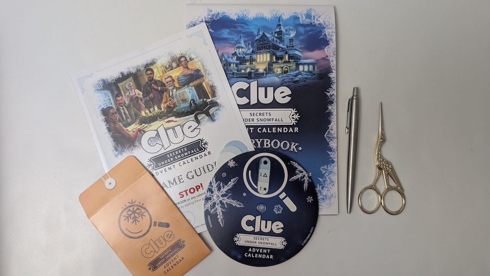 Clue Advent Calendar storybook, plater guide, and a solution wheel beside a pair of scissors and a pen.