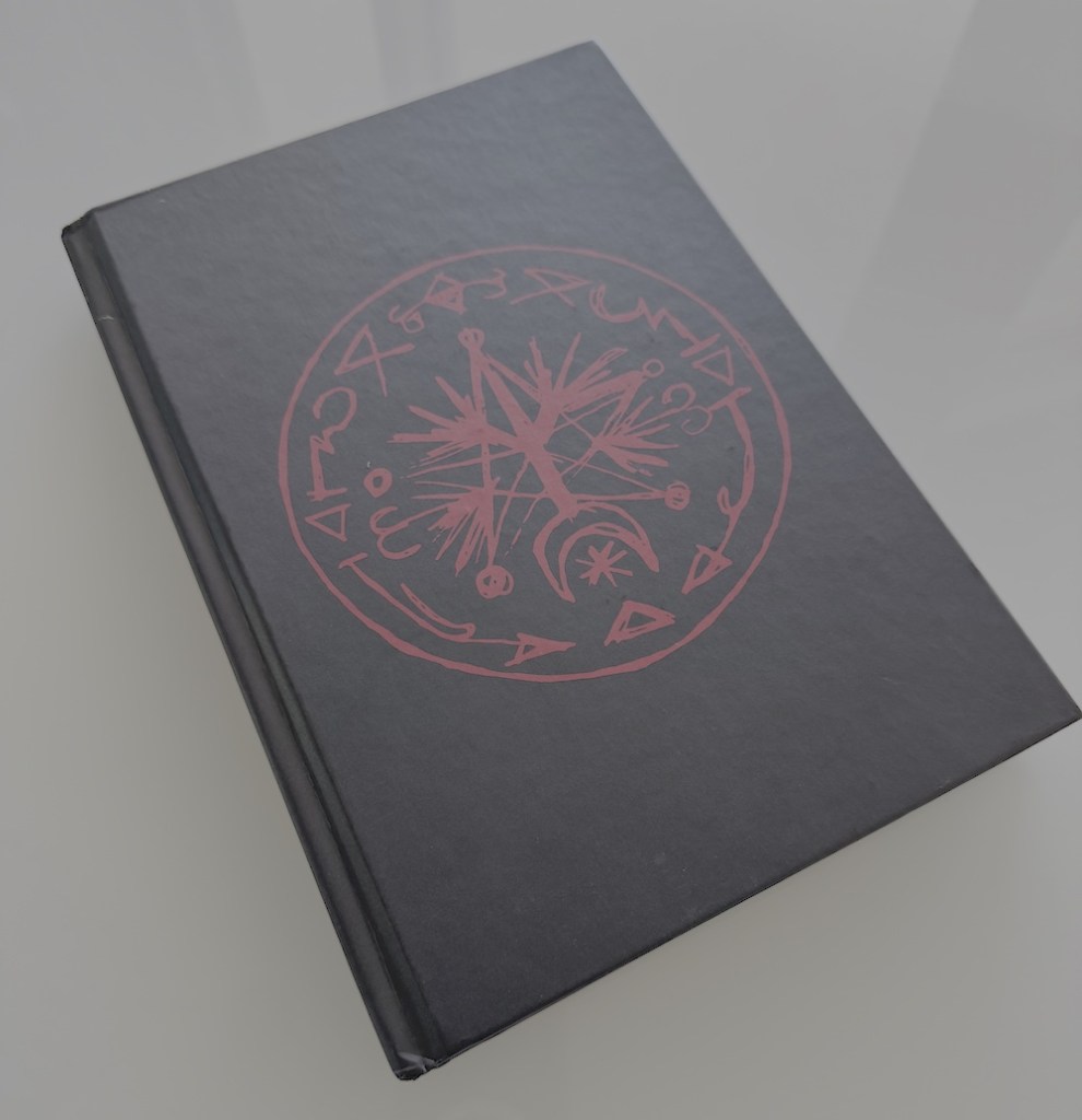 The cover of a black book with a symbol on the front in red.