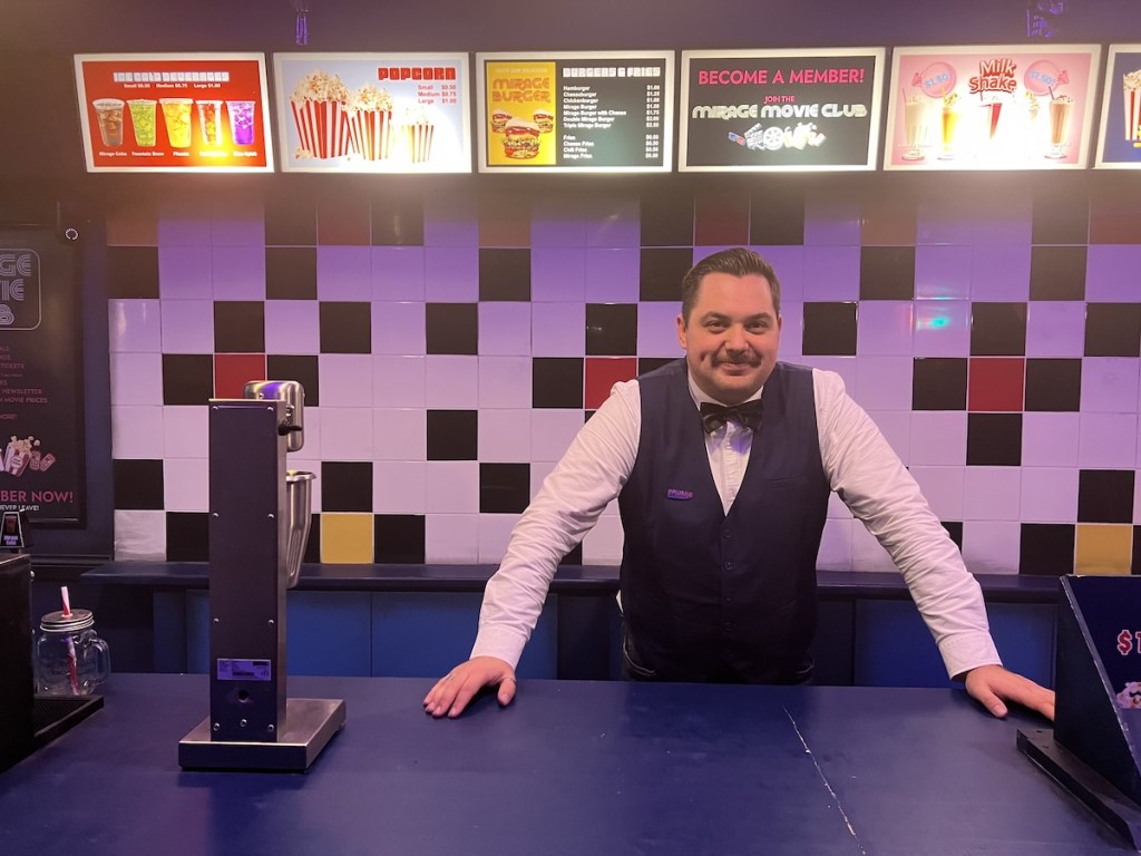 A cinema usher standing behind the food counter in an 80s movie theater.