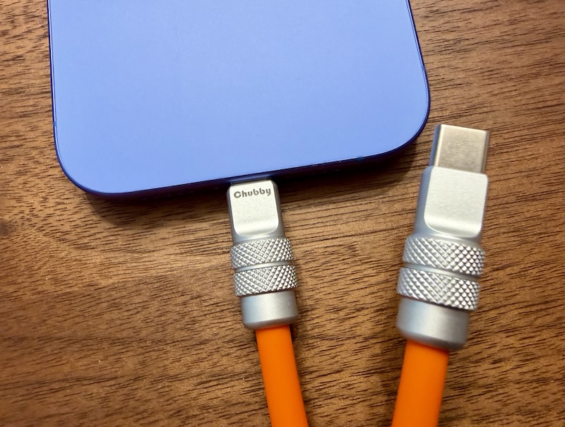 A thiccc USB C cable with chonky connectors. One end is plugged into an iPhone, the other is loose.