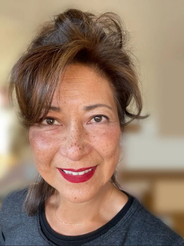 eurasian woman with sideswept bangs, freckles, smiling, wearing red lipstick