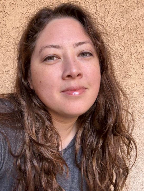 woman with eurasian features, hazel eyes, long wavy brown hair and a gentle smile.