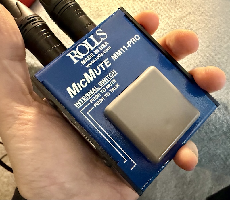 A hand holding a blue metal box labeled Mic Mute with a gray switch.