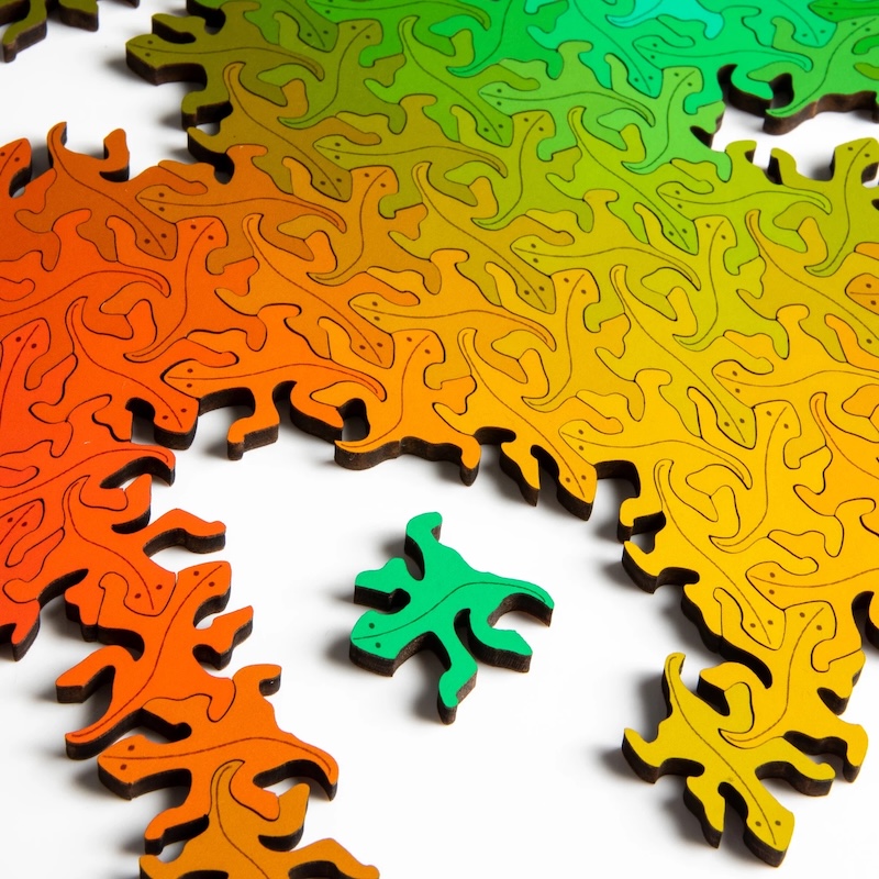 A laser-cut wooden jigsaw puzzle made up of the same lizard shaped pieces that connect infinitely with one another. The only difference between the pieces is color and hue.
