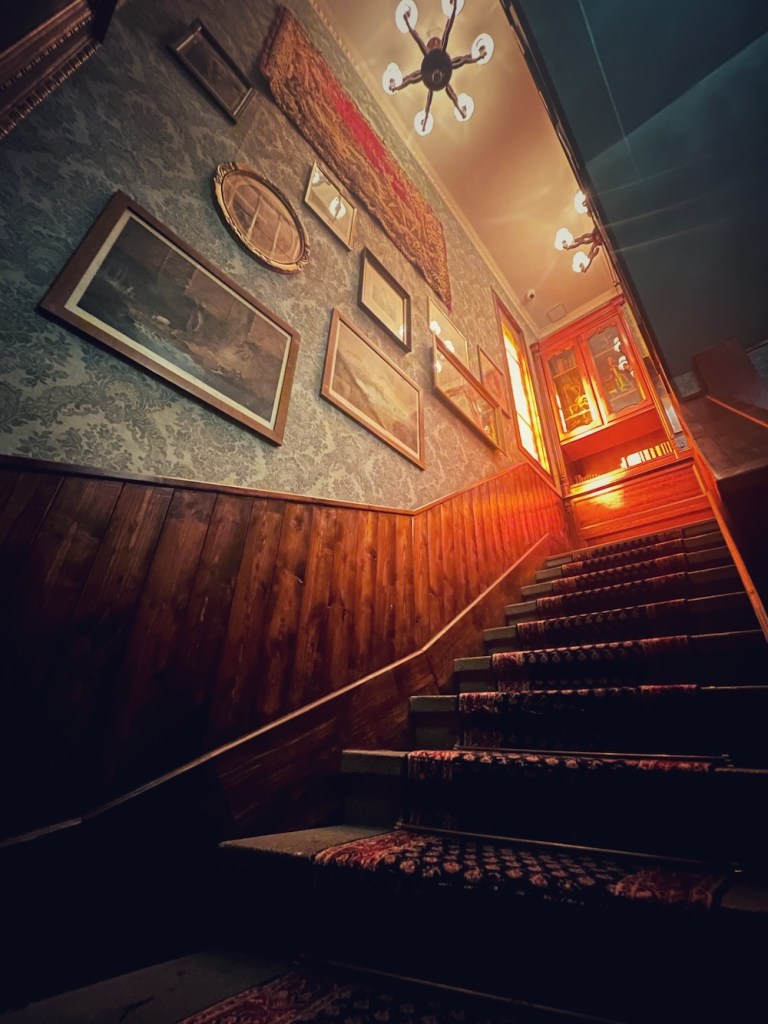 A tall staircase, lined with framed artwork and bright chandeliers hanging high above.