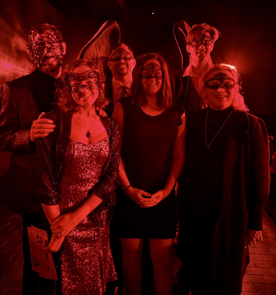 Lisa and David and friends dressed up in sliver, white, and black, wearing masks and lit dramatically in red.