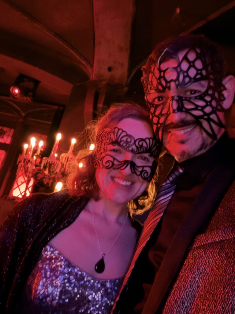 Lisa and David dressed up in sliver and black, wearing intricate, black, laser-cut leather masks.