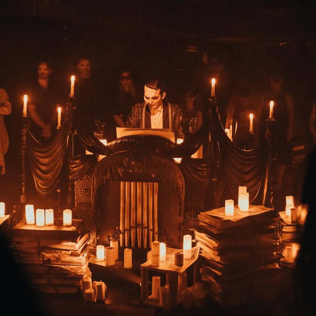 The Phantom playing at a pipe organ, surrounded by candles and masked audience members.