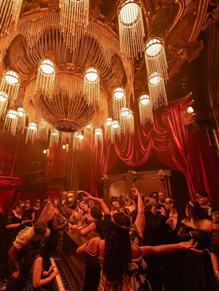 A massive chandelier with masquerade guests looking on.