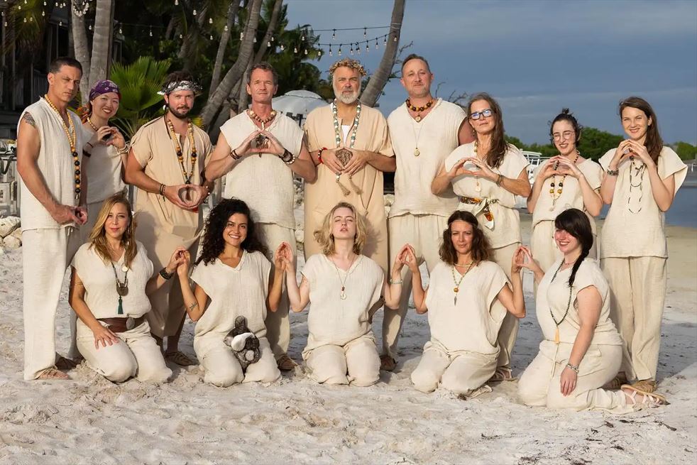 group of people dressed like cult members all in white with wooden bead necklaces posed on a beach