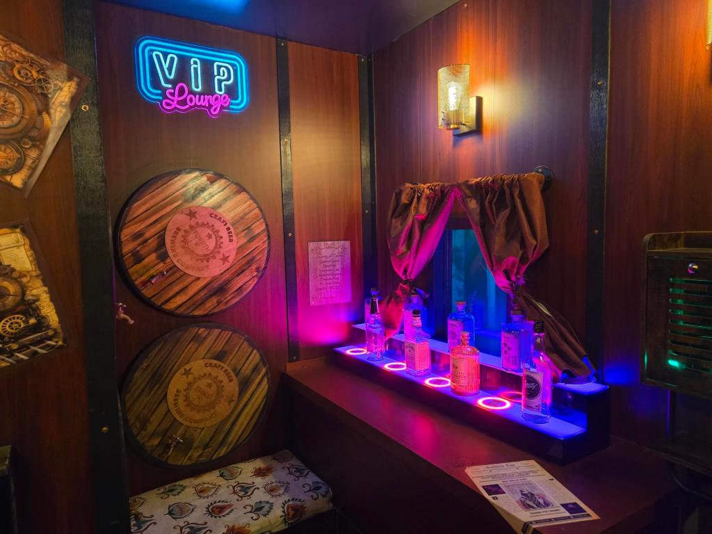 The corner of a wood-paneled VIP lounge with a small wooden shelf containing glowing bottles in front of a curtained window