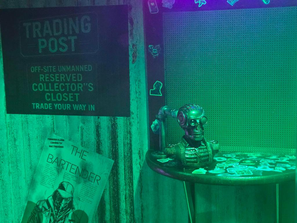 A room in green light. On a small table is a pirate skull and bust. A sign on the wall says "trading post."
