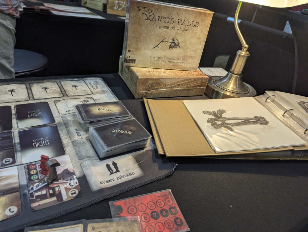 closeup of the game Mantis Falls. on the side is a binder of hand-drawn concept art.