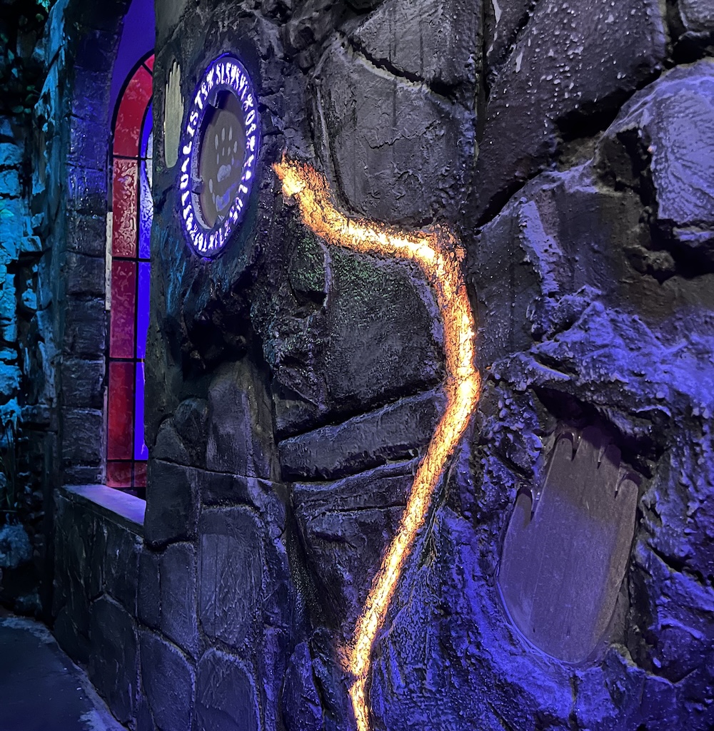 A circle of glowing glyphs in a stone wall. A glowing orange line traces down the stone from the circle of glyphs.