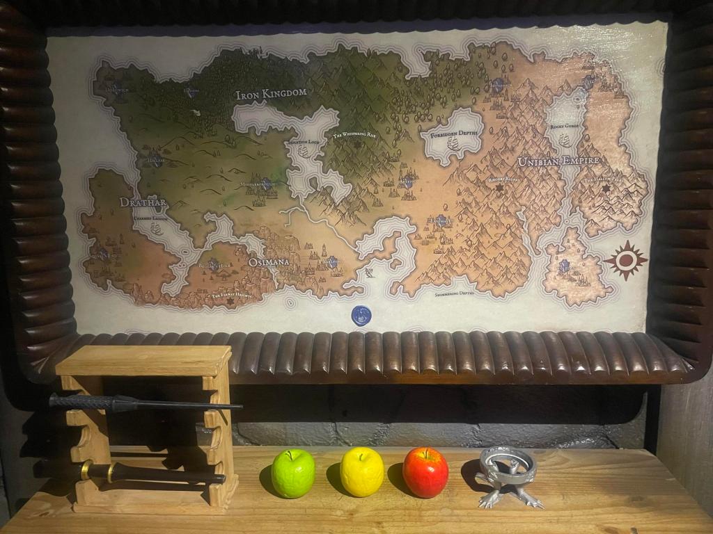 A wall-mounted map of a fantasy kingdom in a large brown frame. There are apples and tools on a shelf below the map.