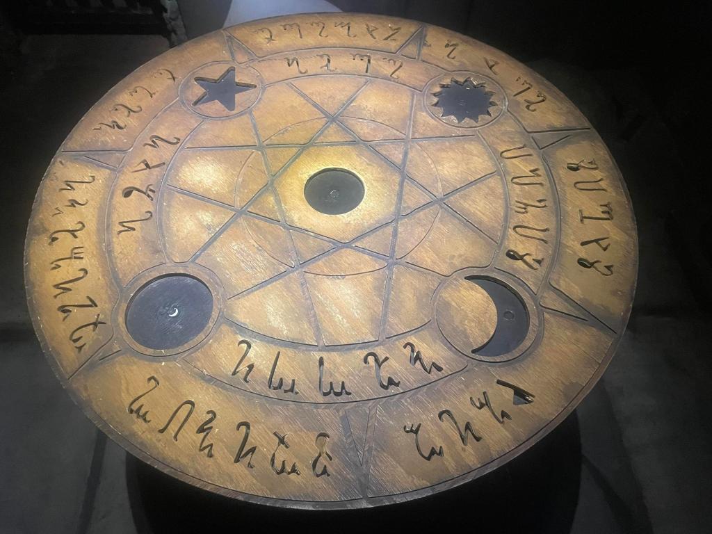 A wooden prop with an unknown script carved into it and different shaped slots (star, circle, sun, moon) to set the correct shaped item atop it.
