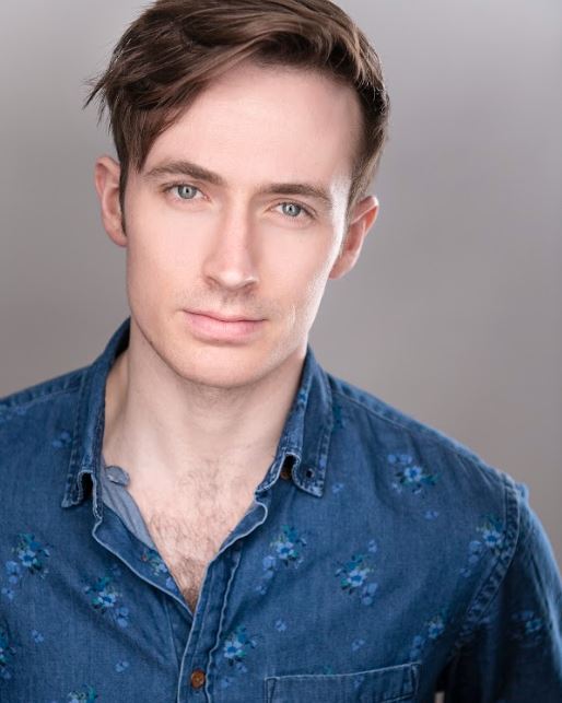 man with sideparted light brown hair, blue eyes, staring intently, in a denim shirt with blue flowers